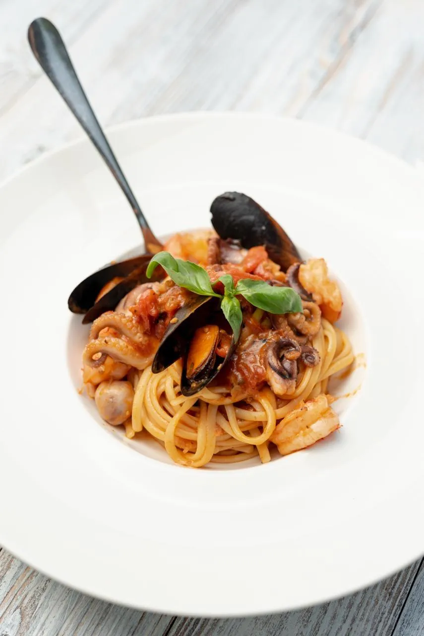 Seafood linguine with mussels, shrimp and squid in tomato sauce, topped with basil