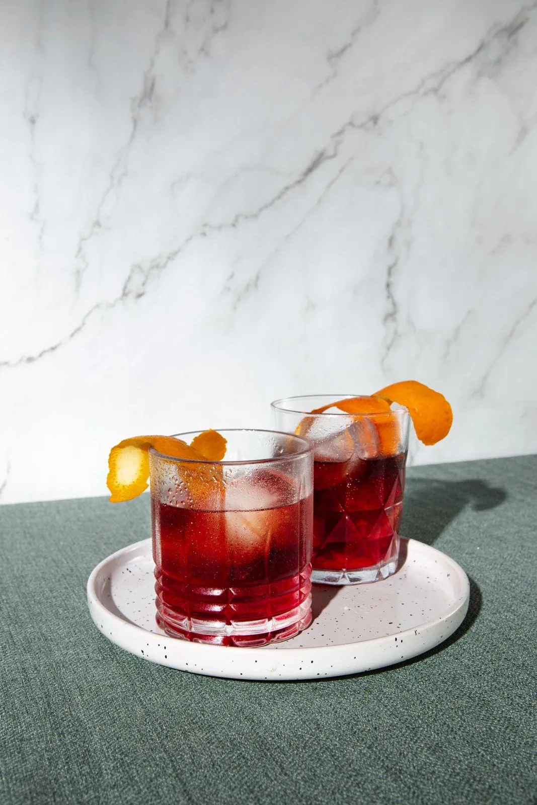 Two negroni cocktails with orange peel on a marble surface
